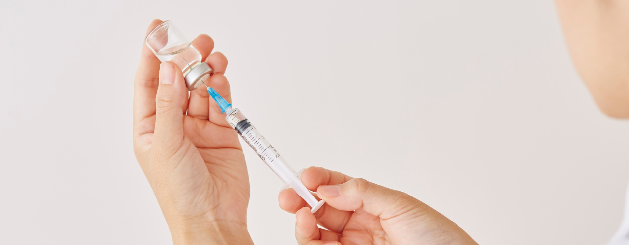 Profissional da saúde preparando seringa com medicamento a partir de um frasco para aplicação injetável de cetoprofeno.