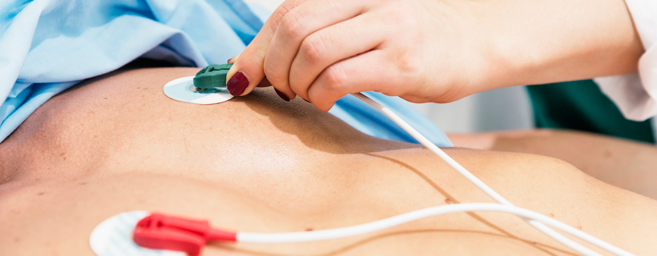 Profissional de saúde posicionando eletrodos ECG no tórax de um paciente para monitorização cardíaca.