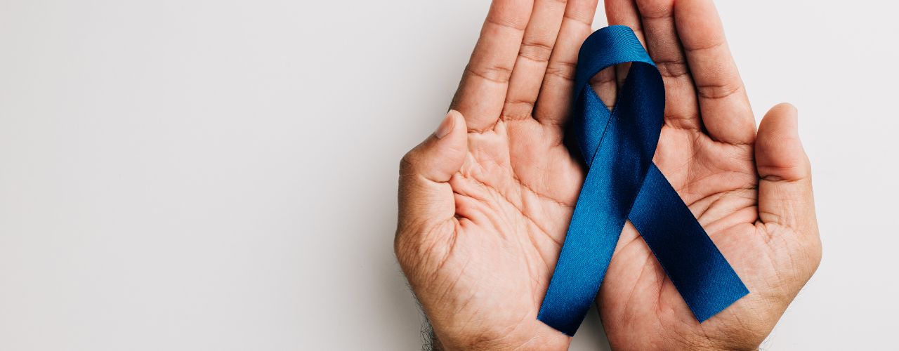 Mãos de homem segurando um laço azul fundo branco claro representando o novembro azul