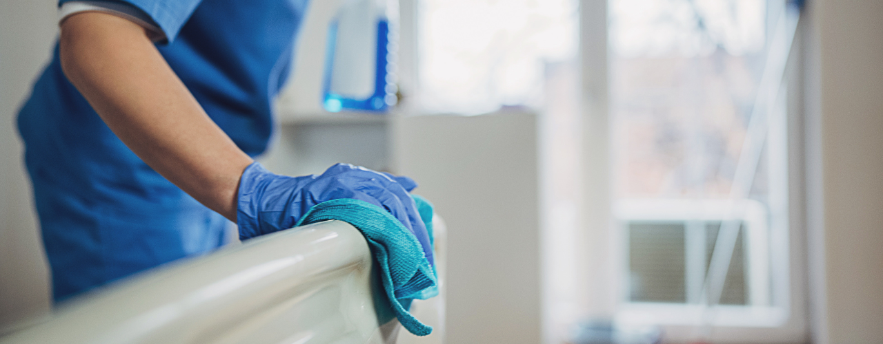 Profissional de saúde utilizando luvas e pano de limpeza para higienizar a estrutura de um leito hospitalar