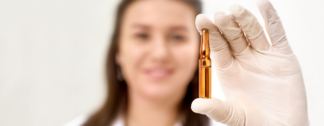 Profissional da saúde, usando luvas descartáveis, segurando uma ampola de medicamento em destaque