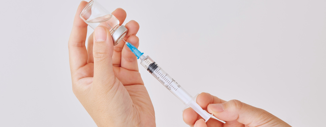 Mãos preparando uma seringa com solução injetável, representando o uso da gentamicina no tratamento de infecções graves.