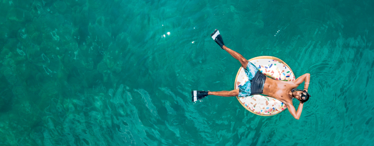 
                Imagem aérea de uma pessoa adulta deitada sobre uma boia circular na água, utilizando traje de banho.
              