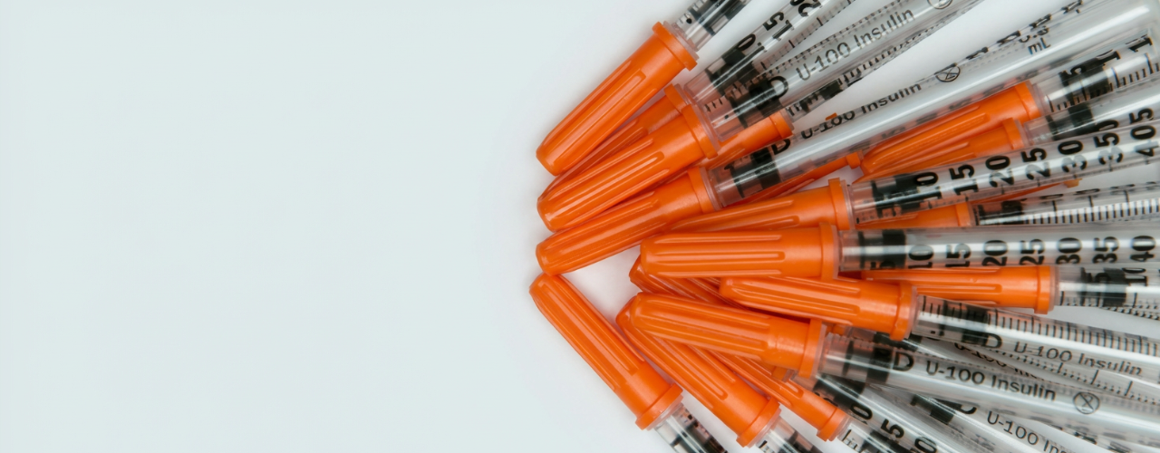 
                Imagem com seringas de insulina U-100 alinhadas, com protetores laranja, destacando a graduação em UI e ml sobre fundo claro.
              