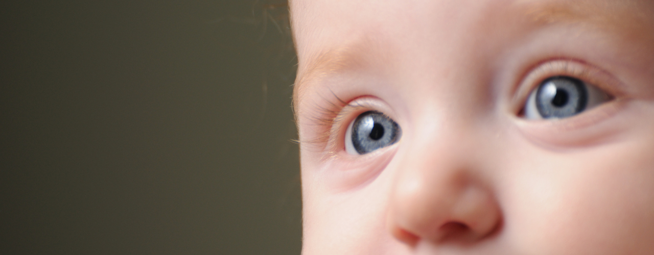 Close-up do rosto de um bebê com foco nos olhos azuis. Destaca detalhes da íris, cílios e da região periocular.