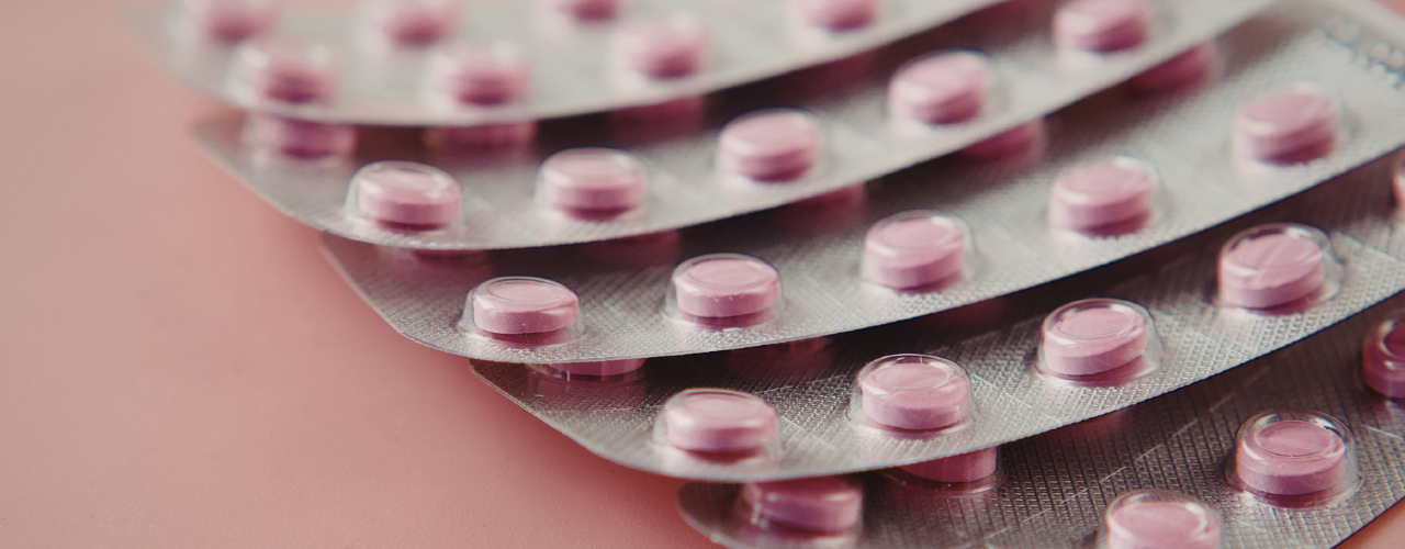 Cartelas de Dramin B6 em cima de um fundo rosa. Comprimidos rosa em cartela prata de alumínio.