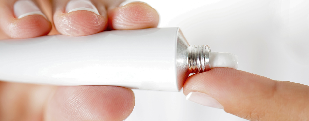 Pessoa aplicando pomada dermatológica colagenase com cloranfenicol na ponta do dedo para tratamento de feridas na pele.